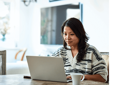 Mid adult woman in her 30s sitting at table and looking at computer, remote working, freelancer, small business