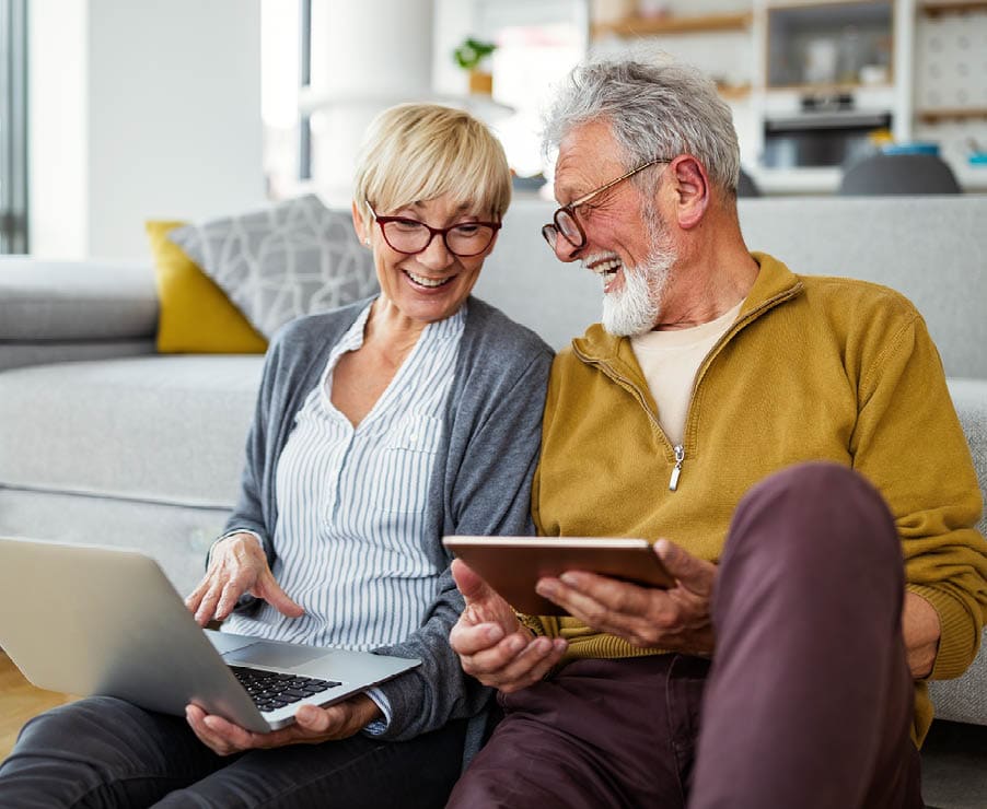 Middle aged man and woman smiling at each other while holding computer and tablet 