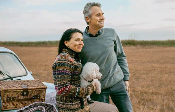 Man and Women holding poodle looking to the distance while on a picnic