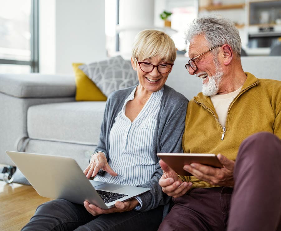 Middle aged man and woman smiling at each other while holding computer and tablet 