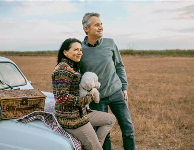 Middle-aged man and women holding a poodle on a picnic looking in the distance.