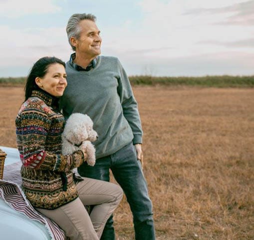 Middle-aged man and women holding a poodle on a picnic looking in the distance.