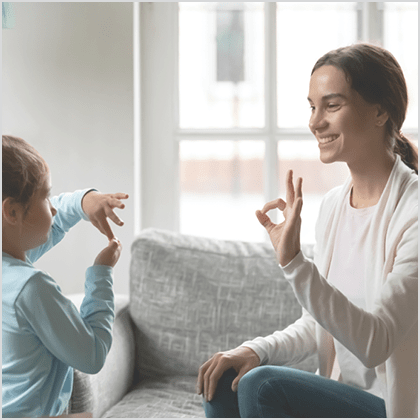 Smiling young Caucasian mom and little daughter make hand gesture learn speak sign language at home, happy mother or nanny practice nonverbal talk with small disabled girl child, disability concept