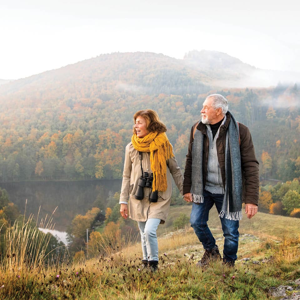 Image of older couple hiking with mountains in background.