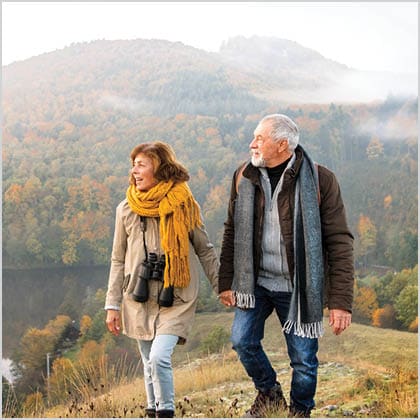 Image of older couple hiking with mountains in background.