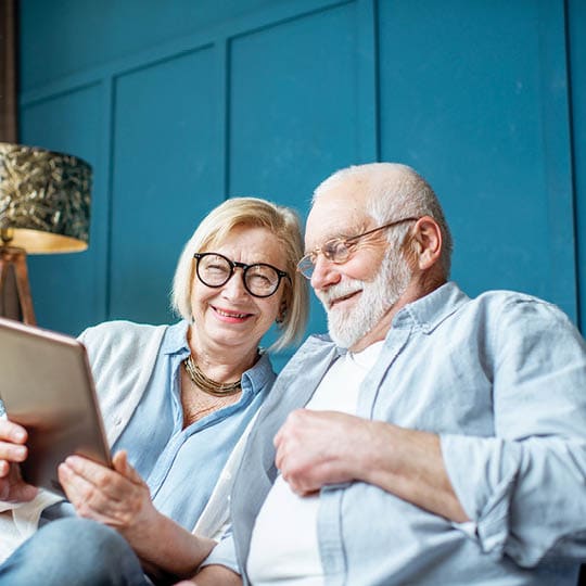 Image of an older couple looking at a tablet together, smiling.