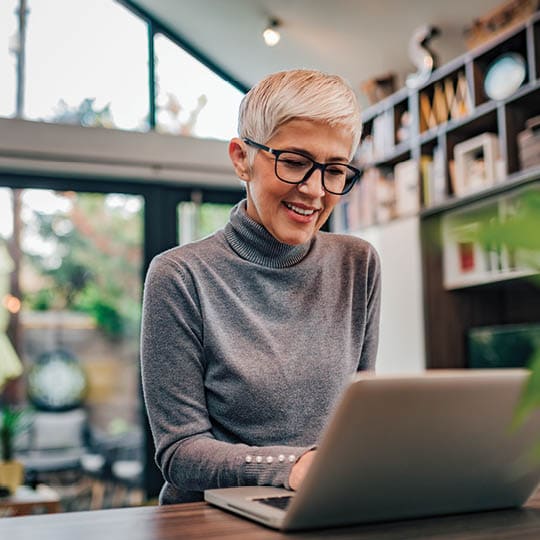 Image of an older woman smiling while on her laptop.