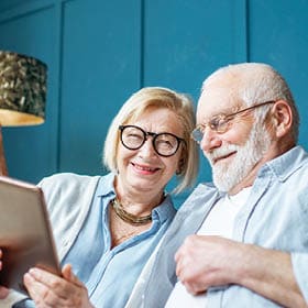 Image of an older couple looking at a tablet together, smiling.