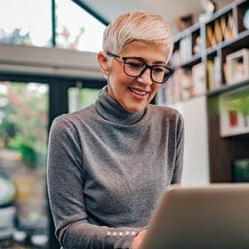Image of an older woman smiling while on her laptop.