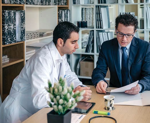 Spain, Asturias, Insurance agent showing health documents to doctor sitting in medical office