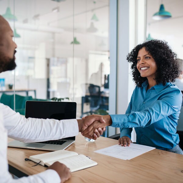 An African American woman is shaking hands across a desk with a male African American financial professional.