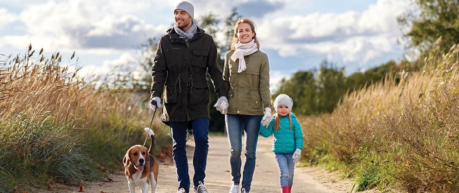 A young couple walking with their daugher and dog. They are all smiling.