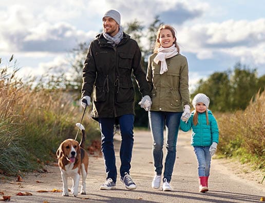 A young couple walking with their daugher and dog. They are all smiling.