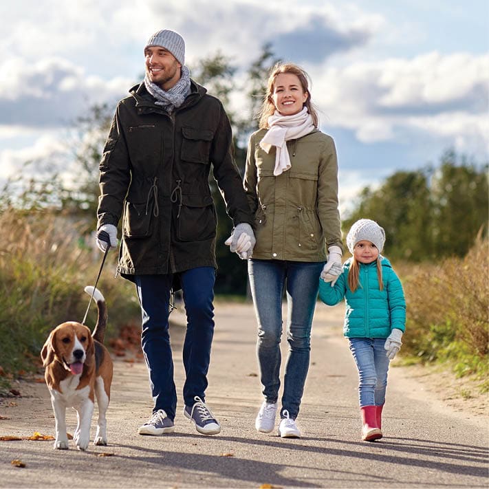 A young couple walking with their daugher and dog. They are all smiling.