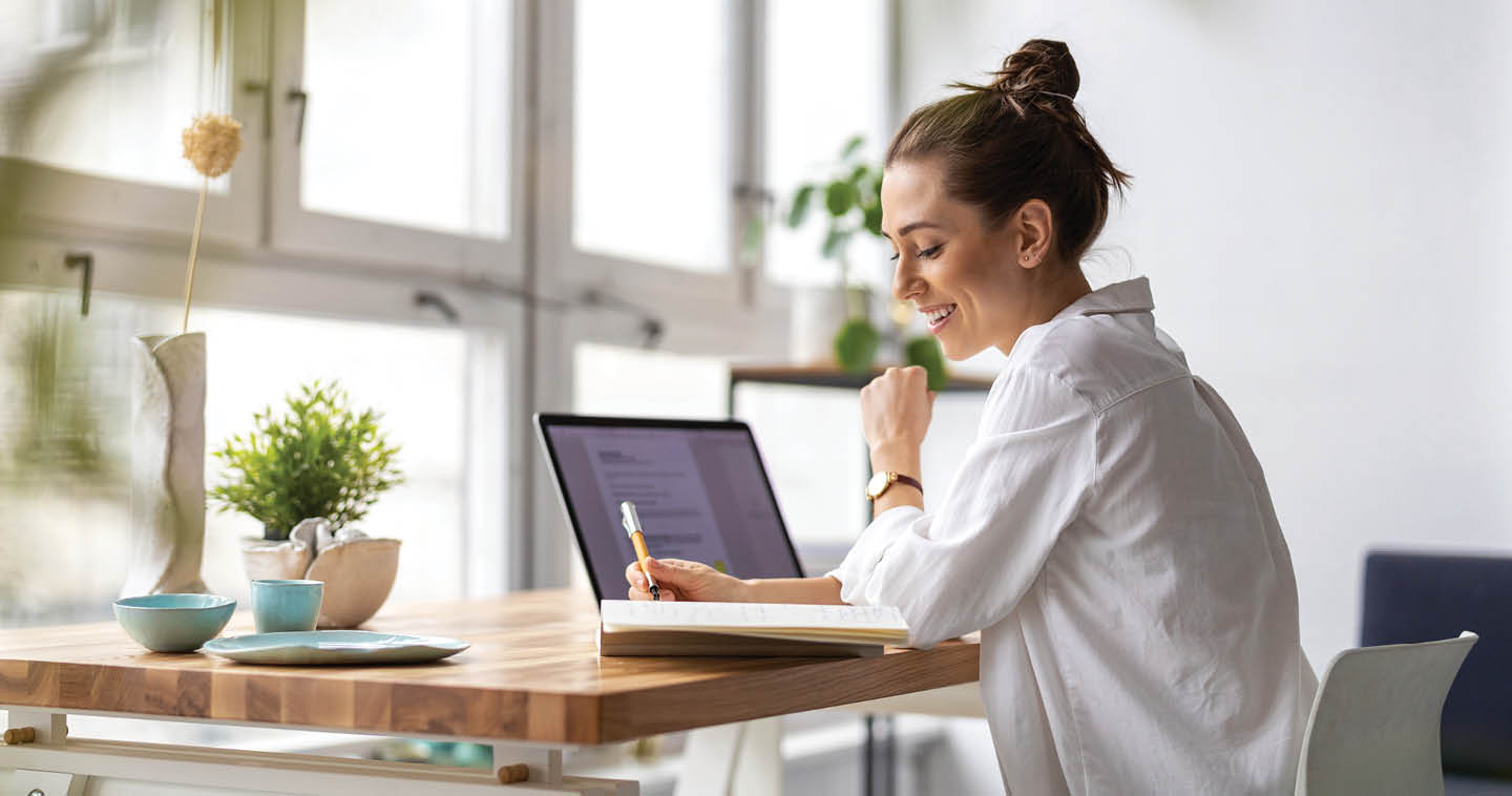 woman with laptop writing in notebook