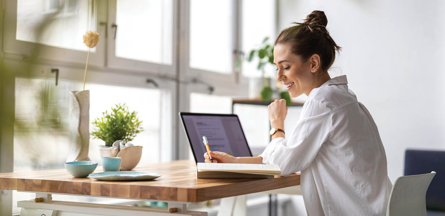 woman with laptop writing in notebook