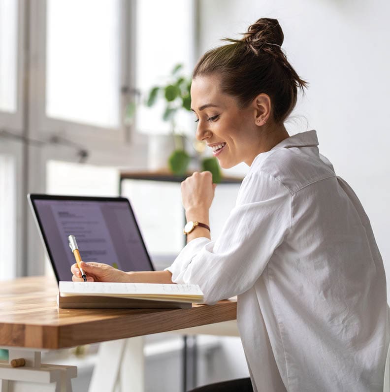 woman with laptop writing in notebook