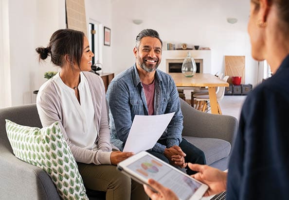 Happy mature couple discussing investments with financial broker during meeting at home. Happy middle eastern man and hispanic woman discussing about financial planning with consultant at home. Financial consultant presenting new investment plan to smiling mature couple at home.